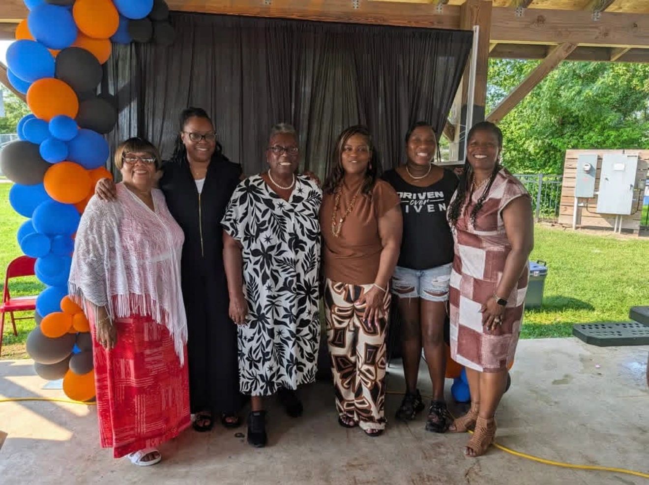 Six women smiling together at an outdoor Driven Over Given community event